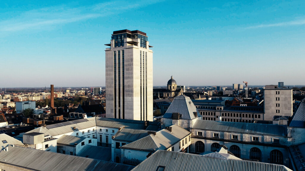 Drone beeld van de UGent met hemelsblauwe lucht en een ochtendzon die schijnt op het gebouw